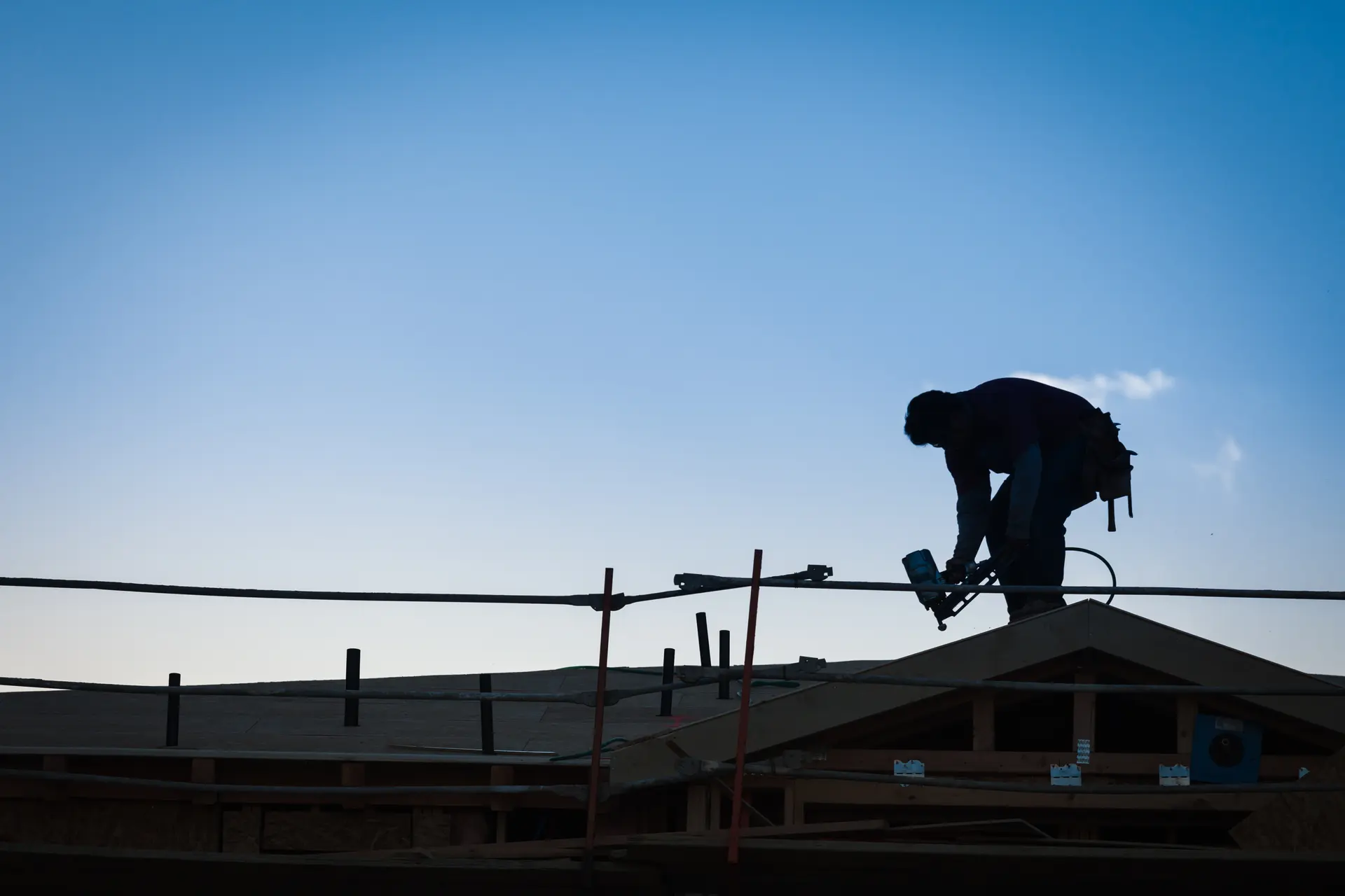 A roofer silhouetted against the sky while working on a roof