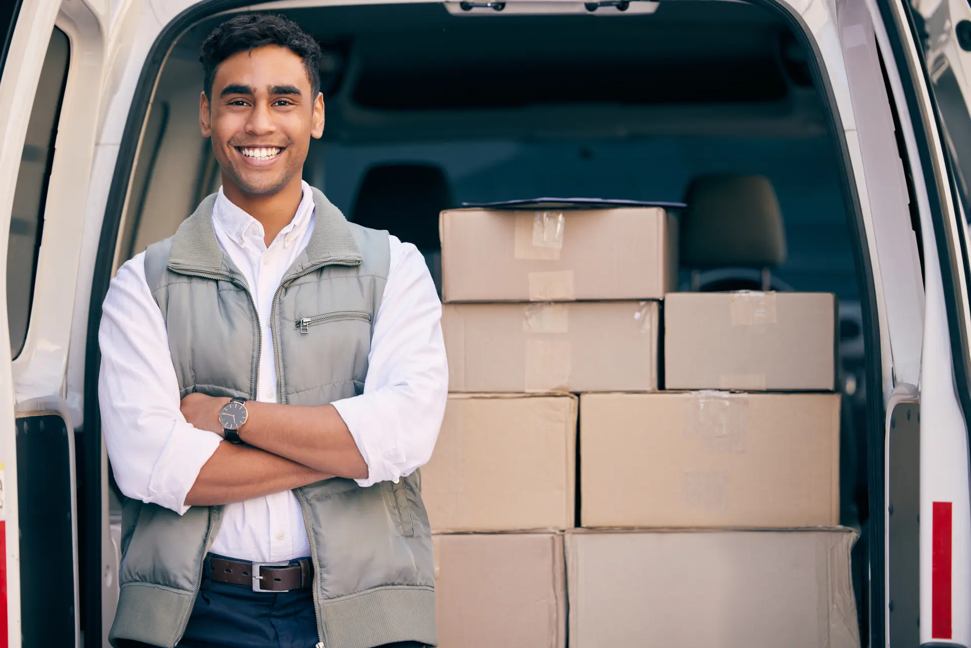 A smiling driver standing at the open doors of a cargo van loaded with boxes